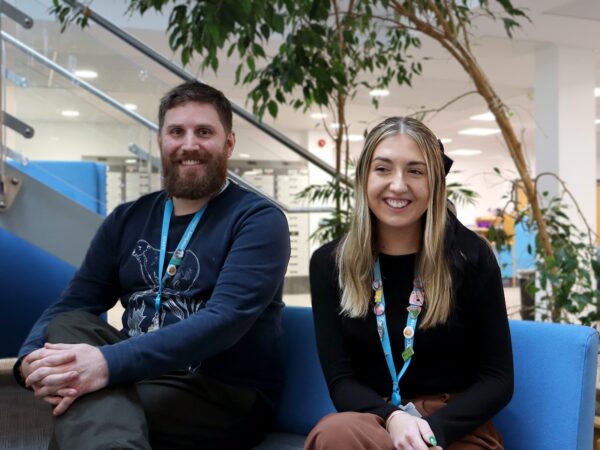 2 people sat on a sofa smiling at the camera