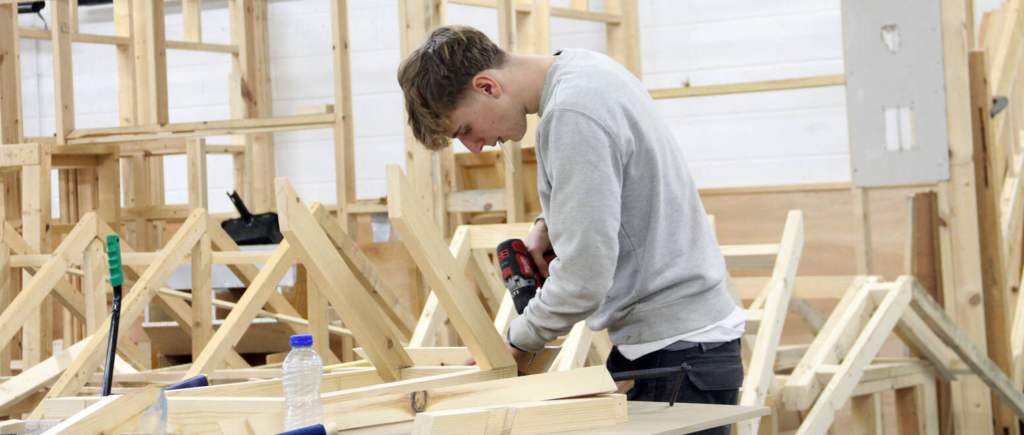 Student drilling into wooden structure on a workbench.
