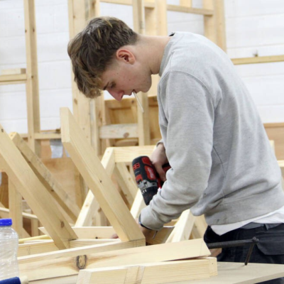 Student drilling into wooden structure on a workbench.