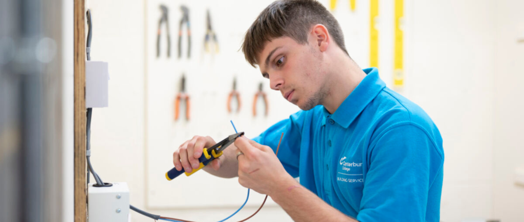 student using pliers on wiring attached to a switchboard.