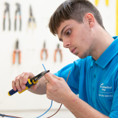 student using pliers on wiring attached to a switchboard.
