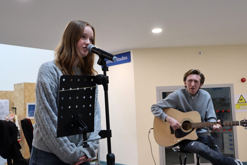 Young lady singing with young man playing guitar.