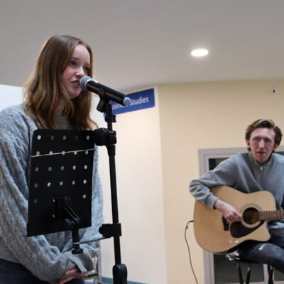 Young lady singing with young man playing guitar.