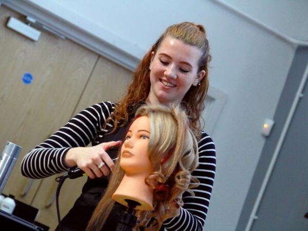 A lady styling the hair of a sally head, hairdressing doll