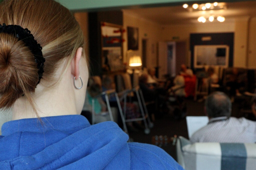 Back of the head of a student with residents of a care home in the background