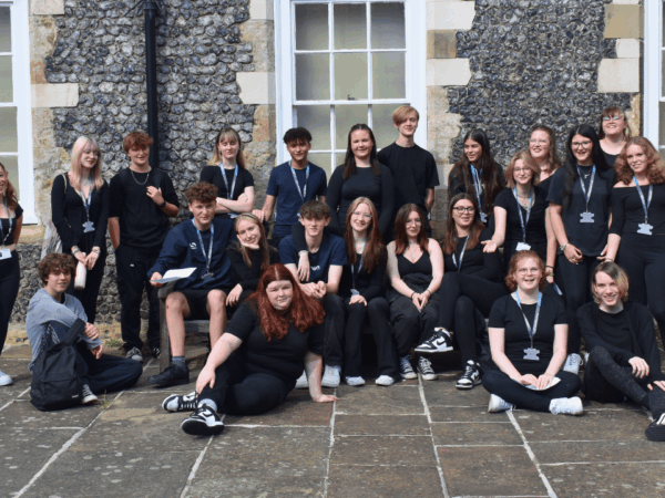 Group photo of students outside a cobbled brick building. They are all wearing dark colours and smiling at the camera.