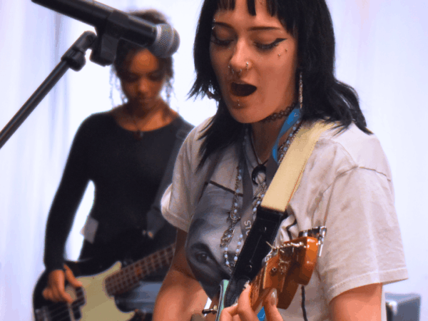 student singing into microphone and playing a guitar, she has black hair.