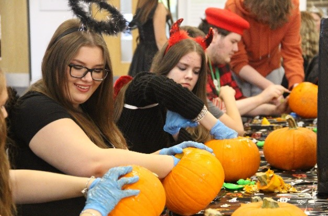 Students carving their pumpkins at a Halloween decorated table.