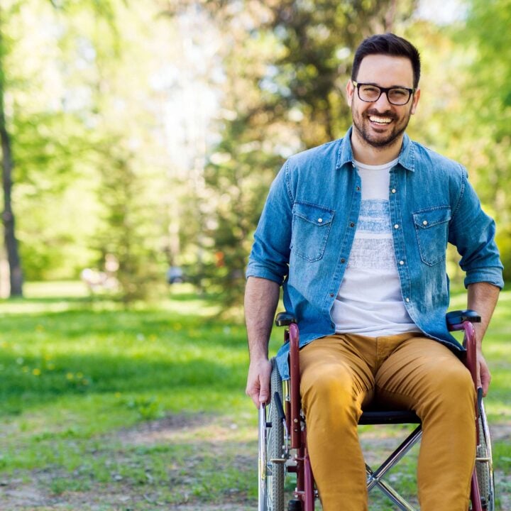 Adult man in wheelchair smiling at camera outside.