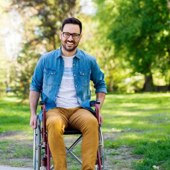 Adult man smiling in a wheelchair outside.