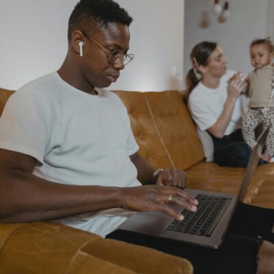 Man working on sofa with woman and baby in background