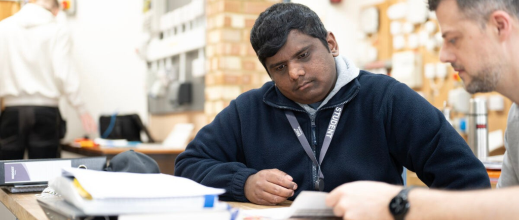 student sitting in electrical workshop with lecturer looking at textbooks,