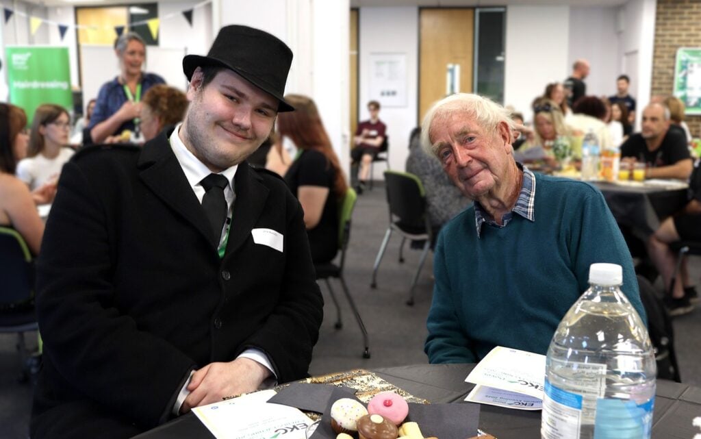 A student and his grandad, both smiling at the camera