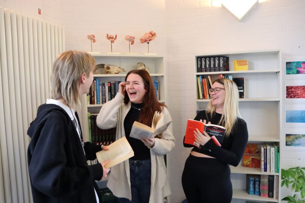 3 young people holding books laughing