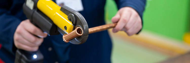 student holding a cutter and cutting a bit of pipe