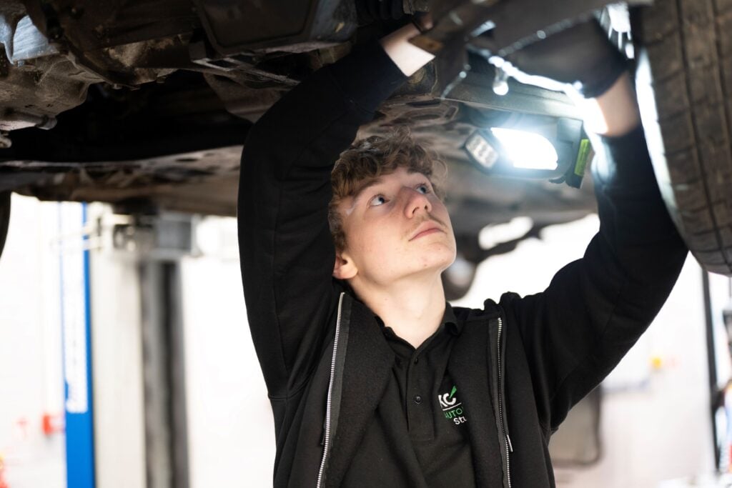 Student shining a torch under a car