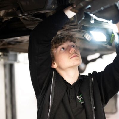 Student shining a torch under a car