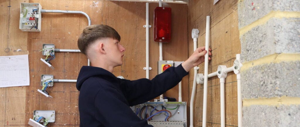student inserting pipes for electrical work onto a brick wall.