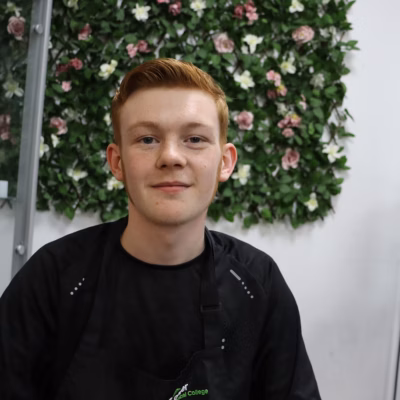 Student has short brown hair, he is smiling at the camera, he is wearing a black top.