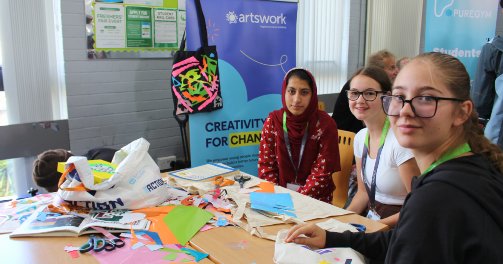 Three students sitting at a table full of colourful vinyl sheets creating their own tote bags.