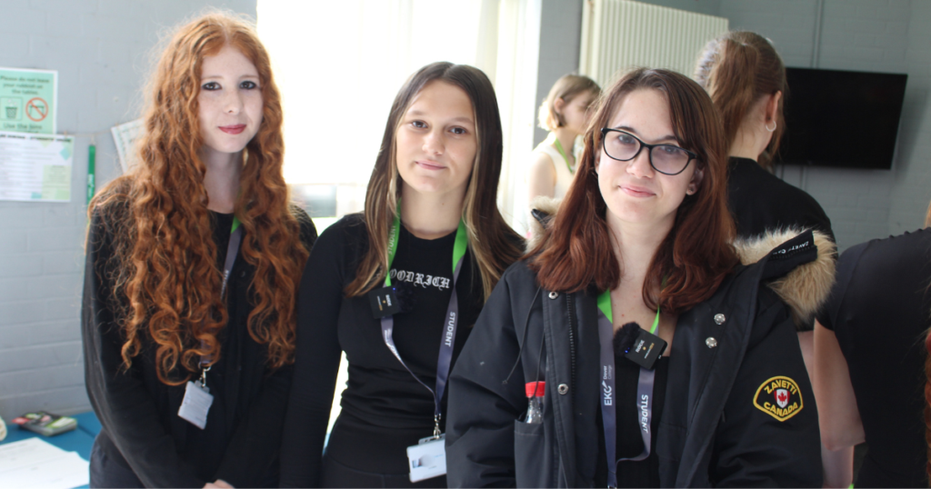 Three students smiling at the camera, one has long red hair, the others are brunette.