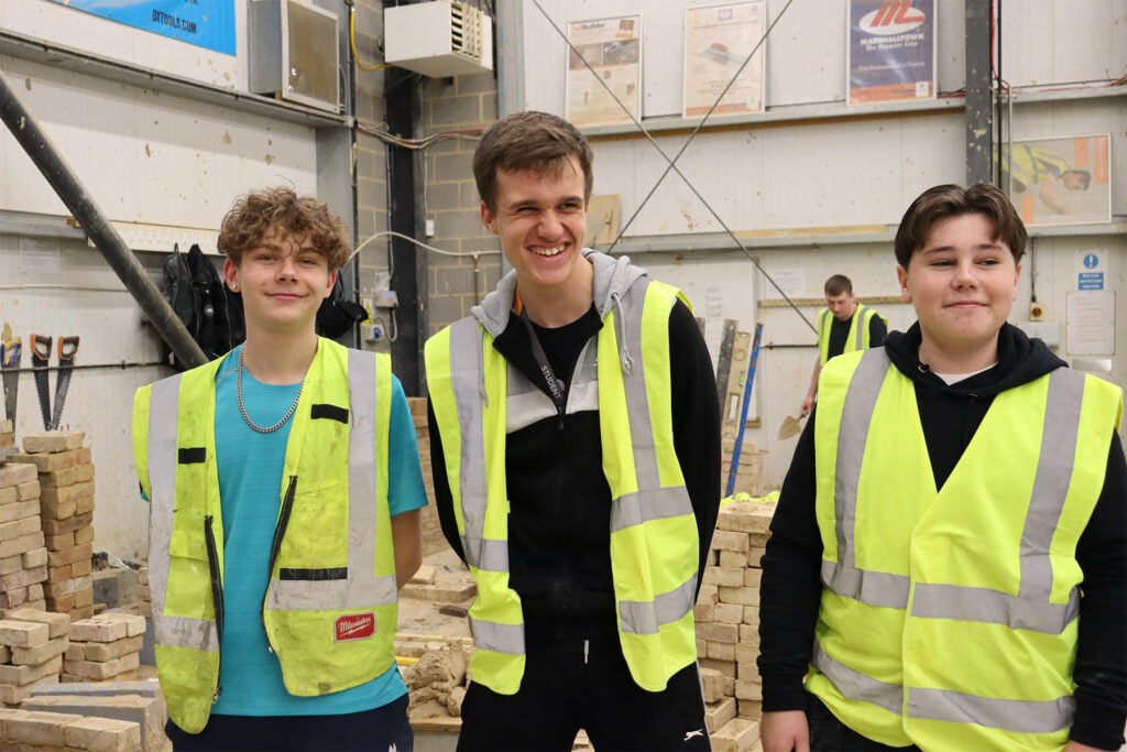 three students stood in a bricklaying workshop