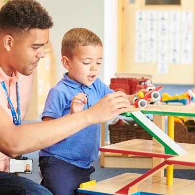 A young adult is helping a boy play with cars in a nursery setting