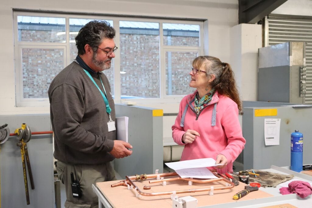 Techer and student in plumbing workshop laughing together