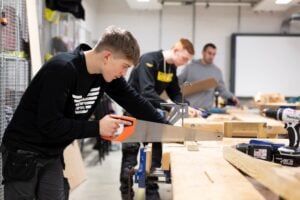Young man sawing some wood on a workbench