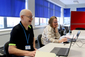 two students in a classroom working on laptops, laughing together