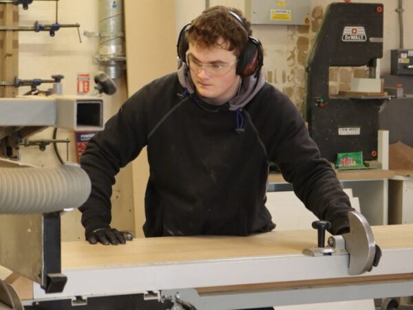 carpentry student sawing a piece of wood with a machine.