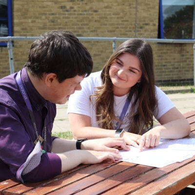 Two students sitting at bench chatting.