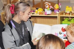 Student reading a children's book to nursery children.
