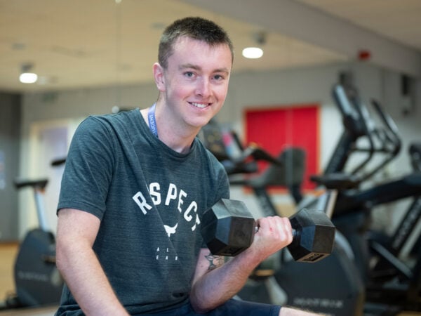 Student smiling holding a weight in his hand in a gym.