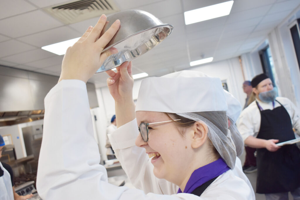 Student holding a mental bowl upside down showing the whisked egg whites holding firm