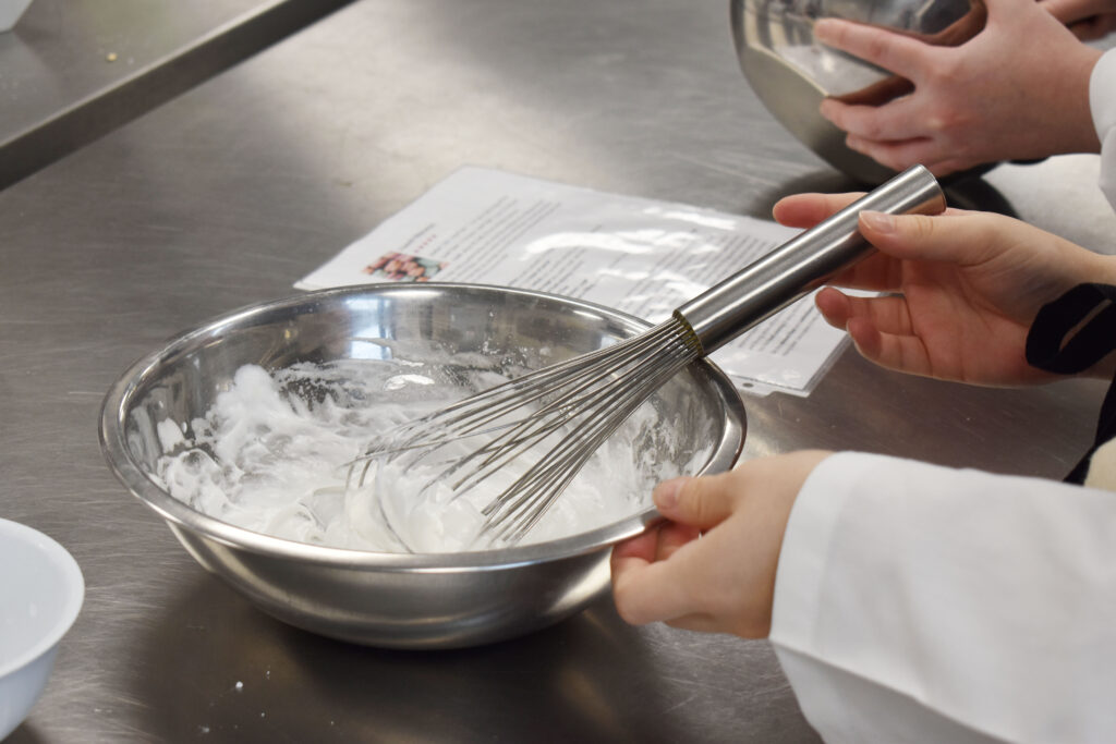 Metal bowl filled with whipped egg whites and whisk
