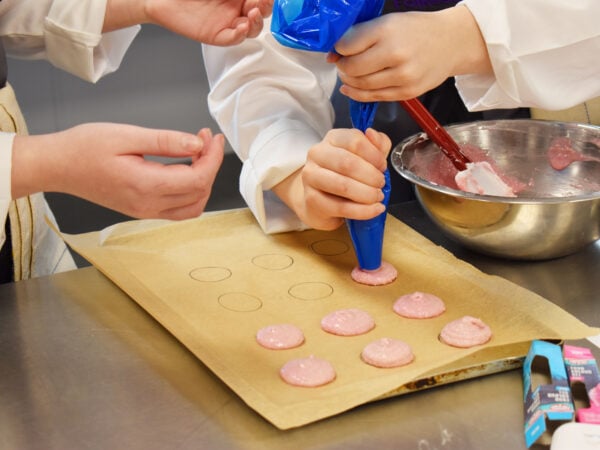 2 students piping the macaron mixture onto baking parchment