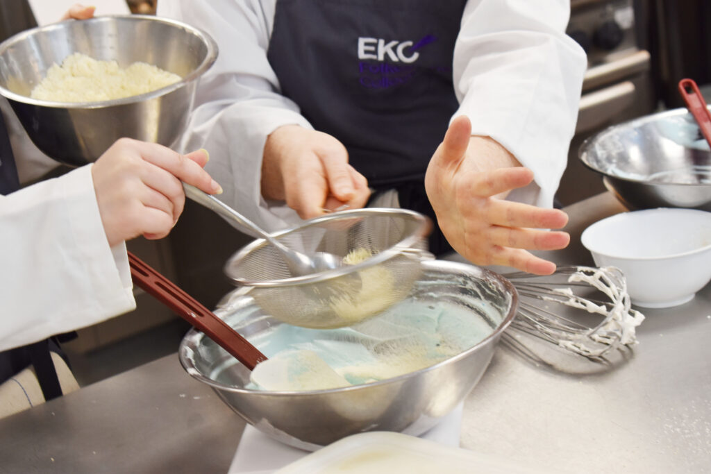 Students using a sieve to add flour to a bowl