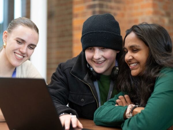 Three students at a table looking at a laptop smiling.