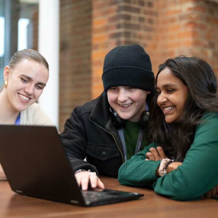 Three students at a table looking at a laptop smiling.