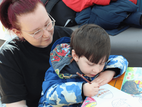 Student sitting with a nursery children who is drawing a picture