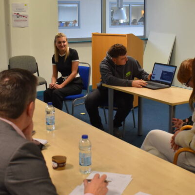 Student presenting to judges on a computer for his new coffee brand idea. Judges looking at his computer screen.