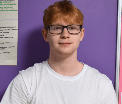 Our student, Liam, smiling at the camera. He is wearing a white t-shirt and has glasses.