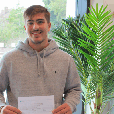 Male student smiling at the camera with his GCSE result paper.