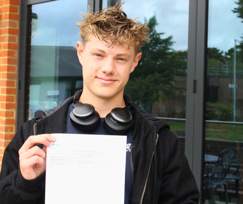 Male student holding up his GCSE results to the camera and smiling.