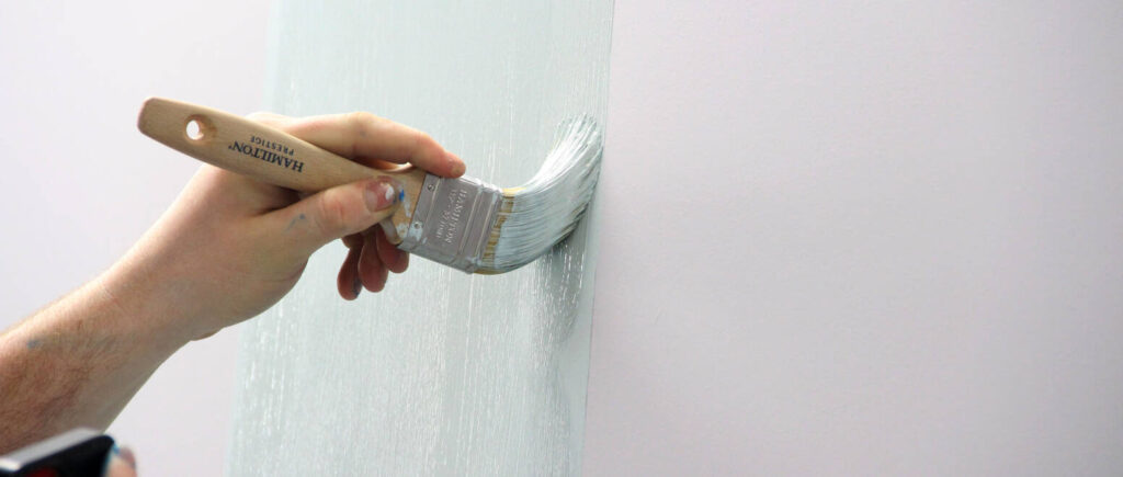 a hand holding a paintbrush and painting a wall in light blue.
