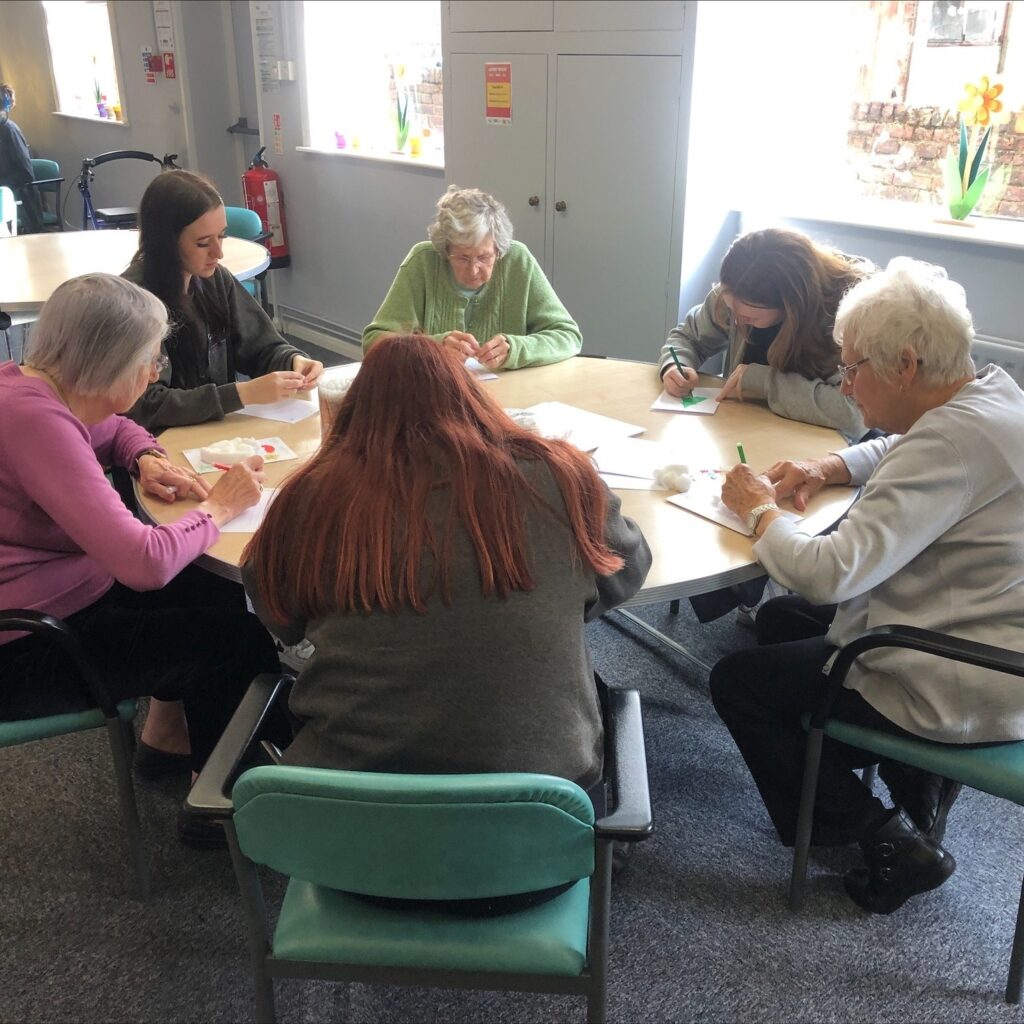students sat around table with elderly residents
