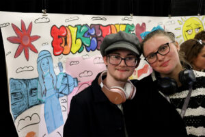 2 art students stood in front of large art display smiling