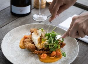 Fish and poached egg dish being cut by a knife and fork on a plate.