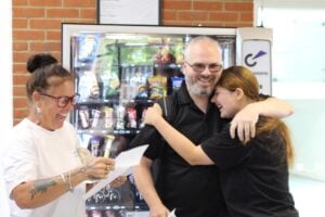 Student hugging her dad and both smiling, mum is reading her results and is very happy.